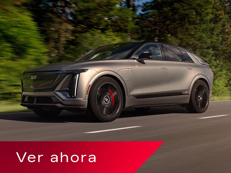 Vista de medio perfil baja de una Cadillac LYRIQ-V circulando por un camino con una hilera de árboles