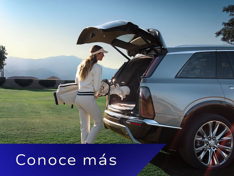 Una mujer coloca una bolsa de golf en la cajuela de una Cadillac VISTIQ en un campo verde