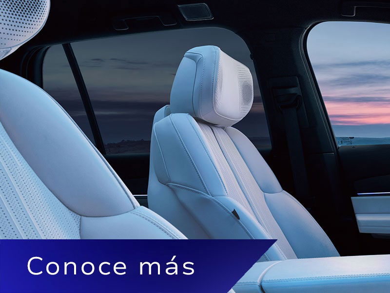 Vista del asiento del pasajero hacia el asiento del conductor y el interior de la primera fila dentro de una Cadillac VISTIQ con el atardecer de fondo