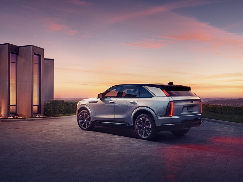 Vista exterior del lado del conductor de Cadillac ESCALADE IQ 2025 estacionada frente a una casa al atardecer