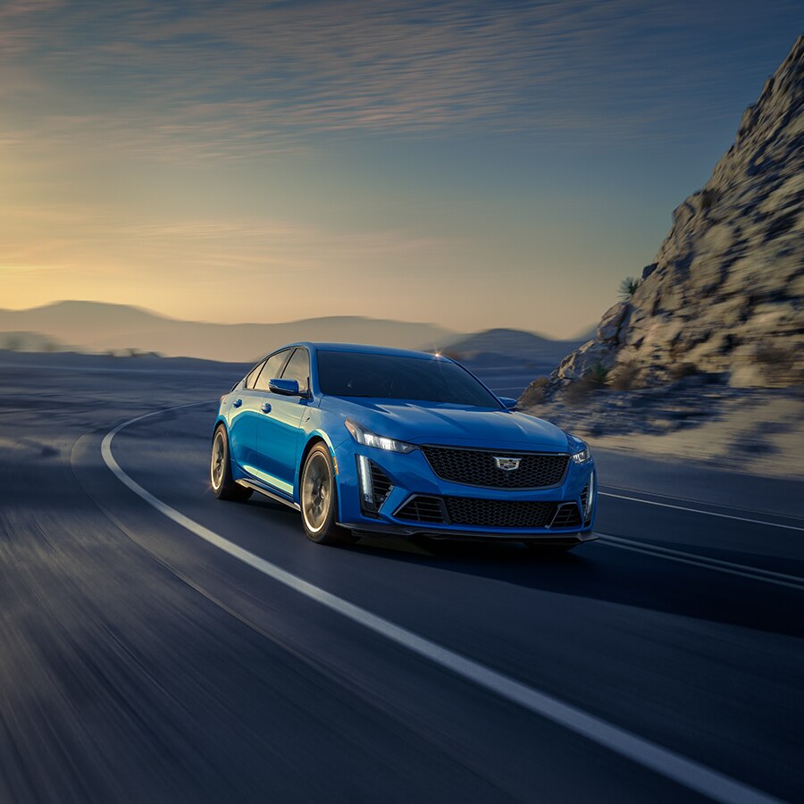 Cadillac CT5-V Blackwing 2024 tomando a toda velocidad una curva en el camino, con montañas de fondo