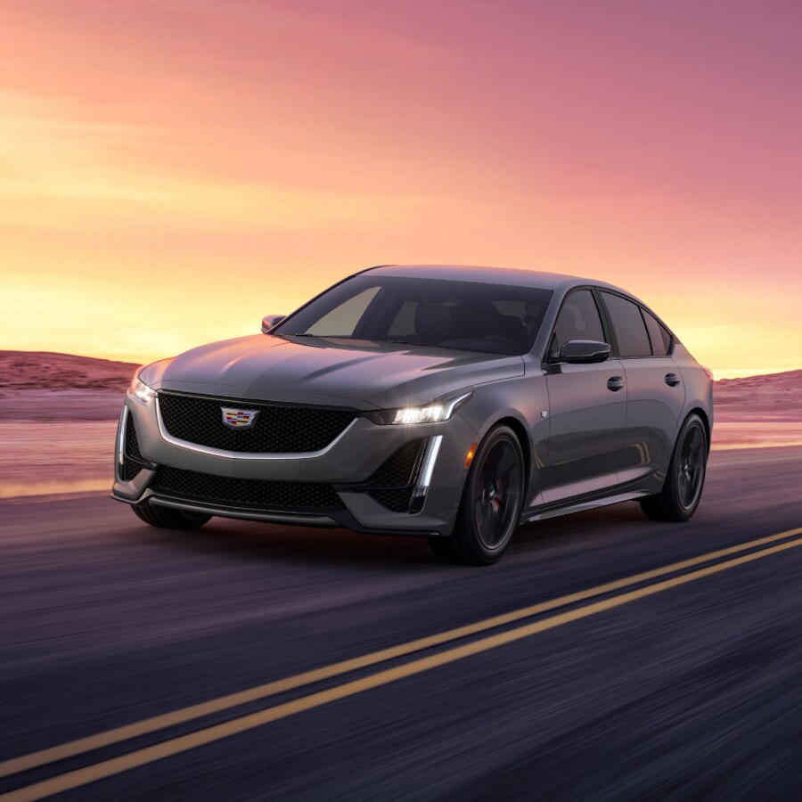 Cadillac CT5 2024 circulando a toda velocidad en un camino al atardecer, con montañas de fondo